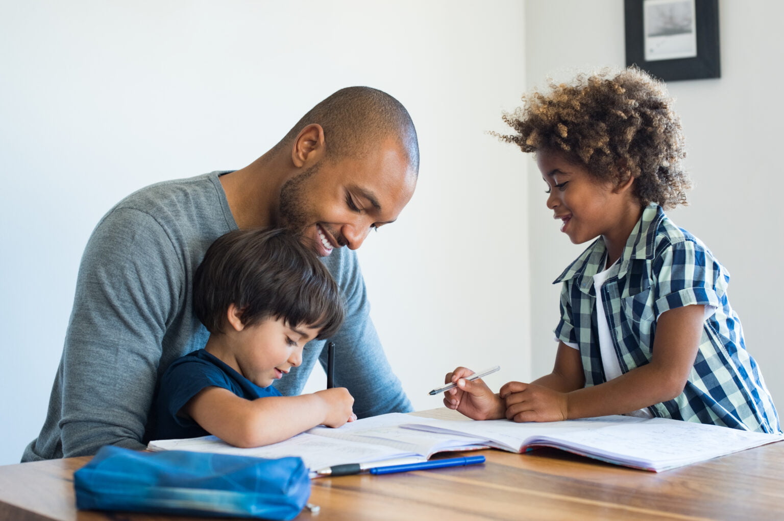 Jovem pai negro ajudando seus duas crianças (meninos) com a lição de casa. Irmãos multiétnicos estudando com o pai em casa. Duas crianças fofas fazendo lição de casa com a ajuda de seus pais amorosos.