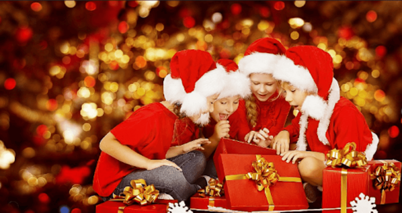 Quatro crianças vestidas com roupas natalinas e chapéus de Papai Noel, abrindo caixas de presente em um ambiente iluminado com luzes de Natal.