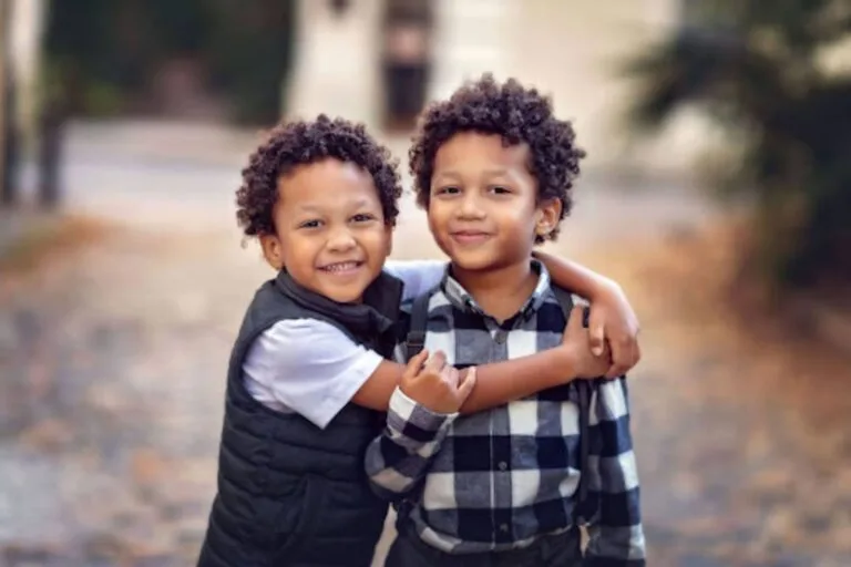 Dois irmãos gêmeos abraçados e sorrindo, representando o vínculo afetivo e a individualidade no desenvolvimento infantil.